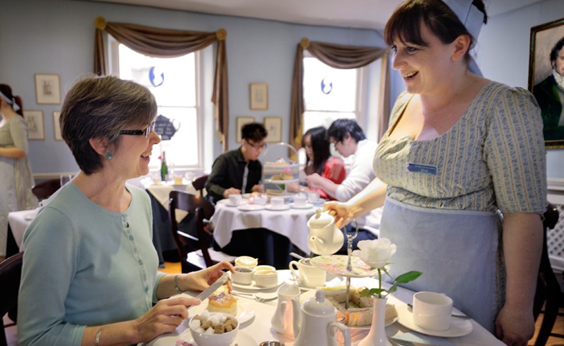 Women in period costume serving tea to woman in the Regency Tea Room